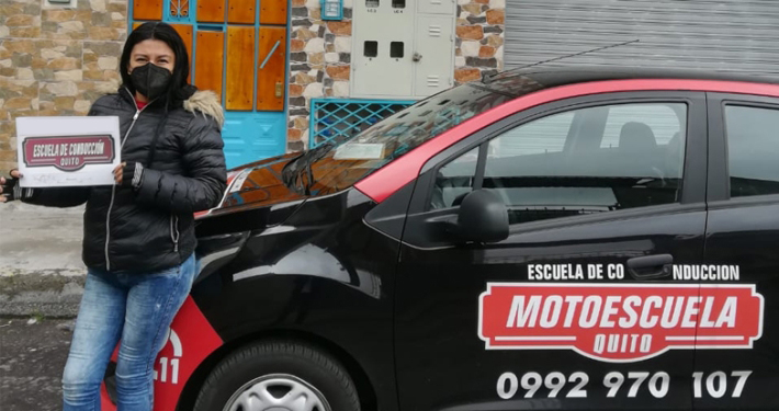 Estudiante graduada junto al vehículo de prácticas de la escuela